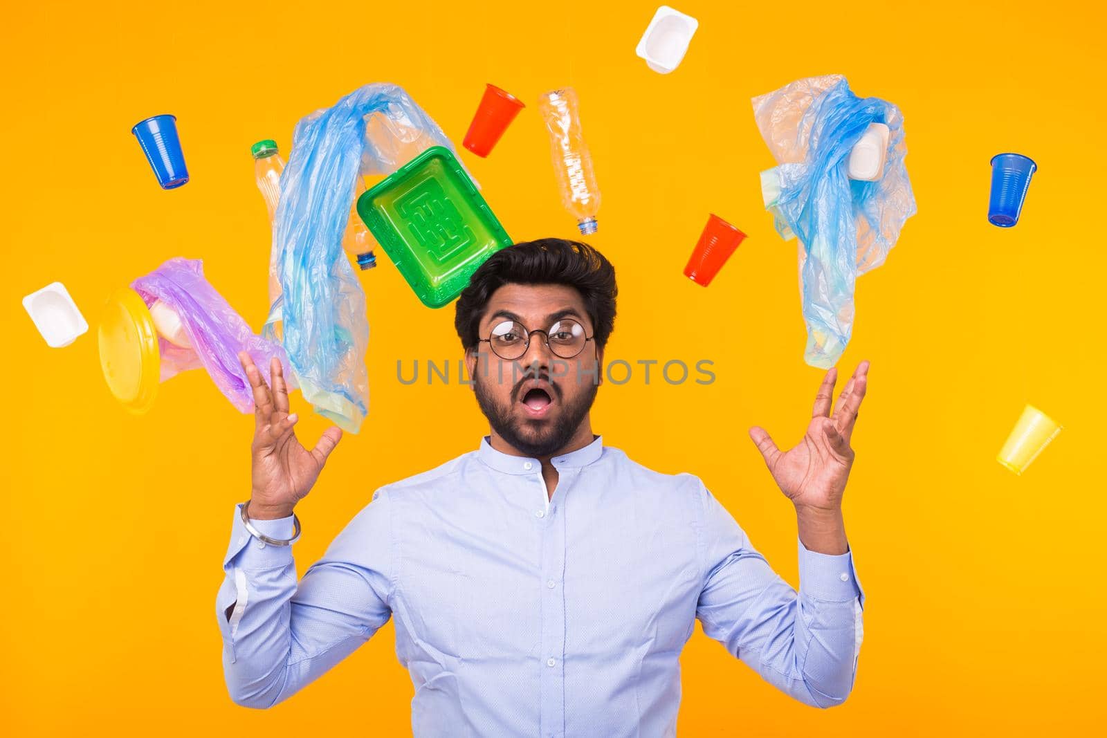 World Environment Day, plastic recycling problem and environmental disaster concept - Terrified Indian man threw up his arms to the sides on yellow background with trash.