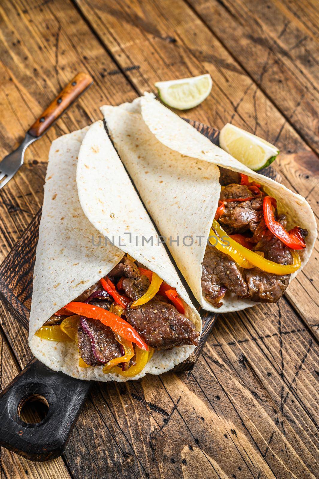 Fajitas Tortilla wrap with beef meat stripes, colored bell pepper and onions and salsa. Wooden background. Top view by Composter