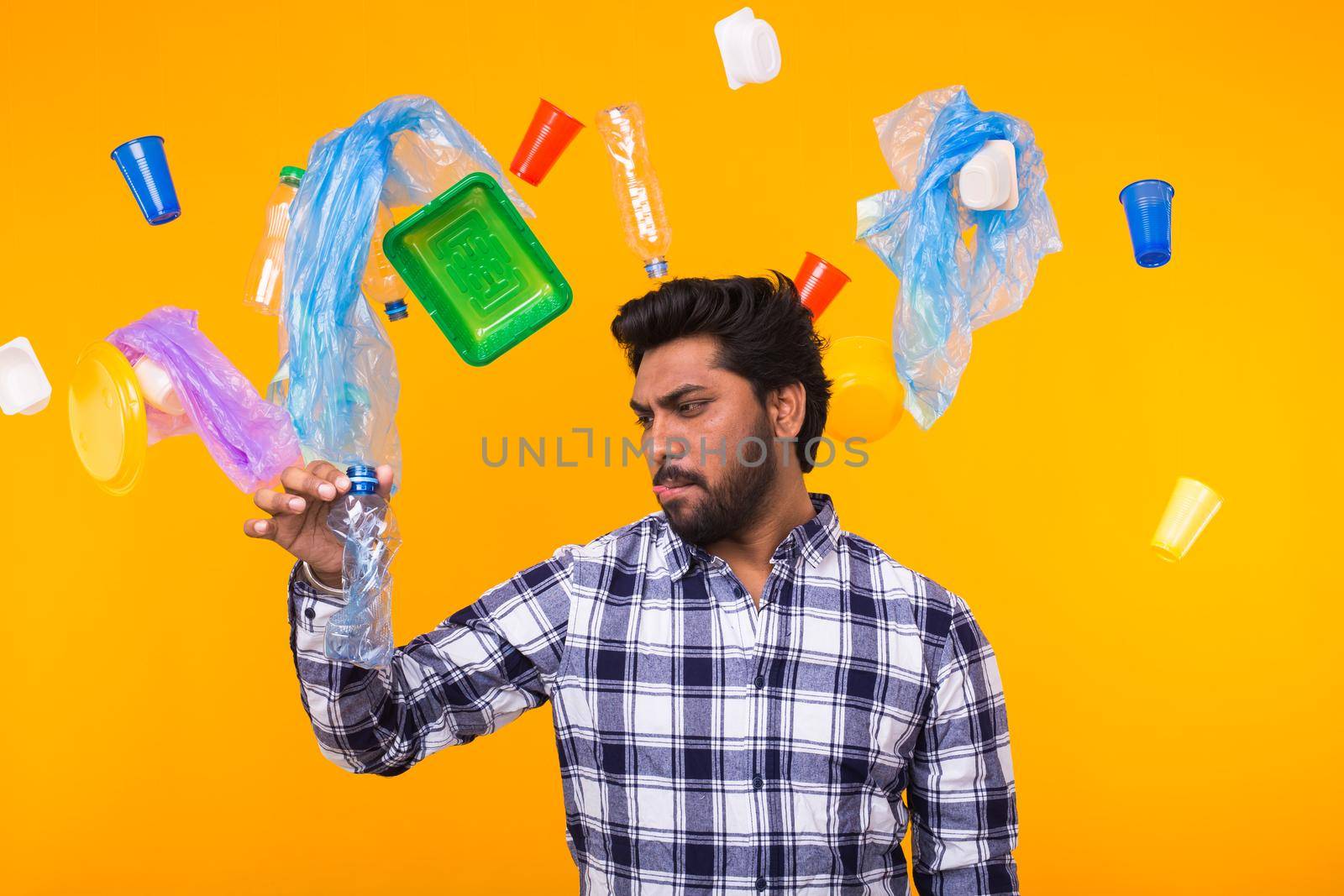 Plastic recycling problem and environmental disaster concept - Indian man hiding from garbage under an umbrella on yellow background.