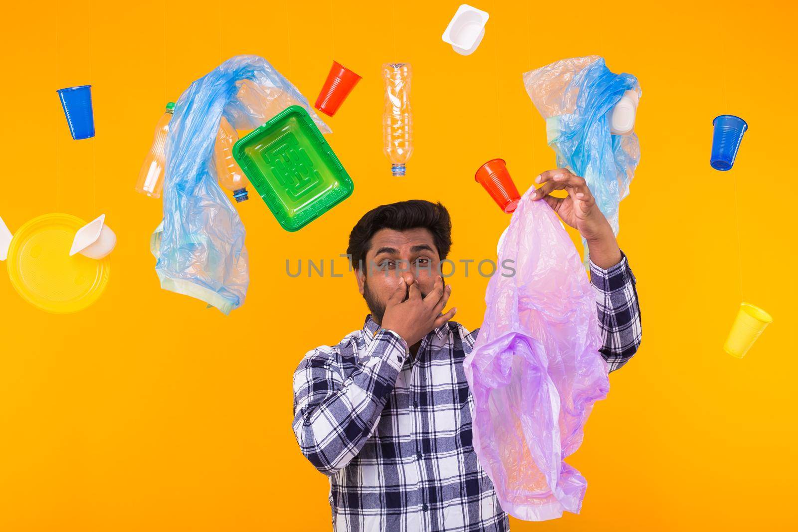 Problem of trash, plastic recycling, pollution and environmental concept - surprised Indian man closing nose because he is felt bad smell from garbage on yellow background