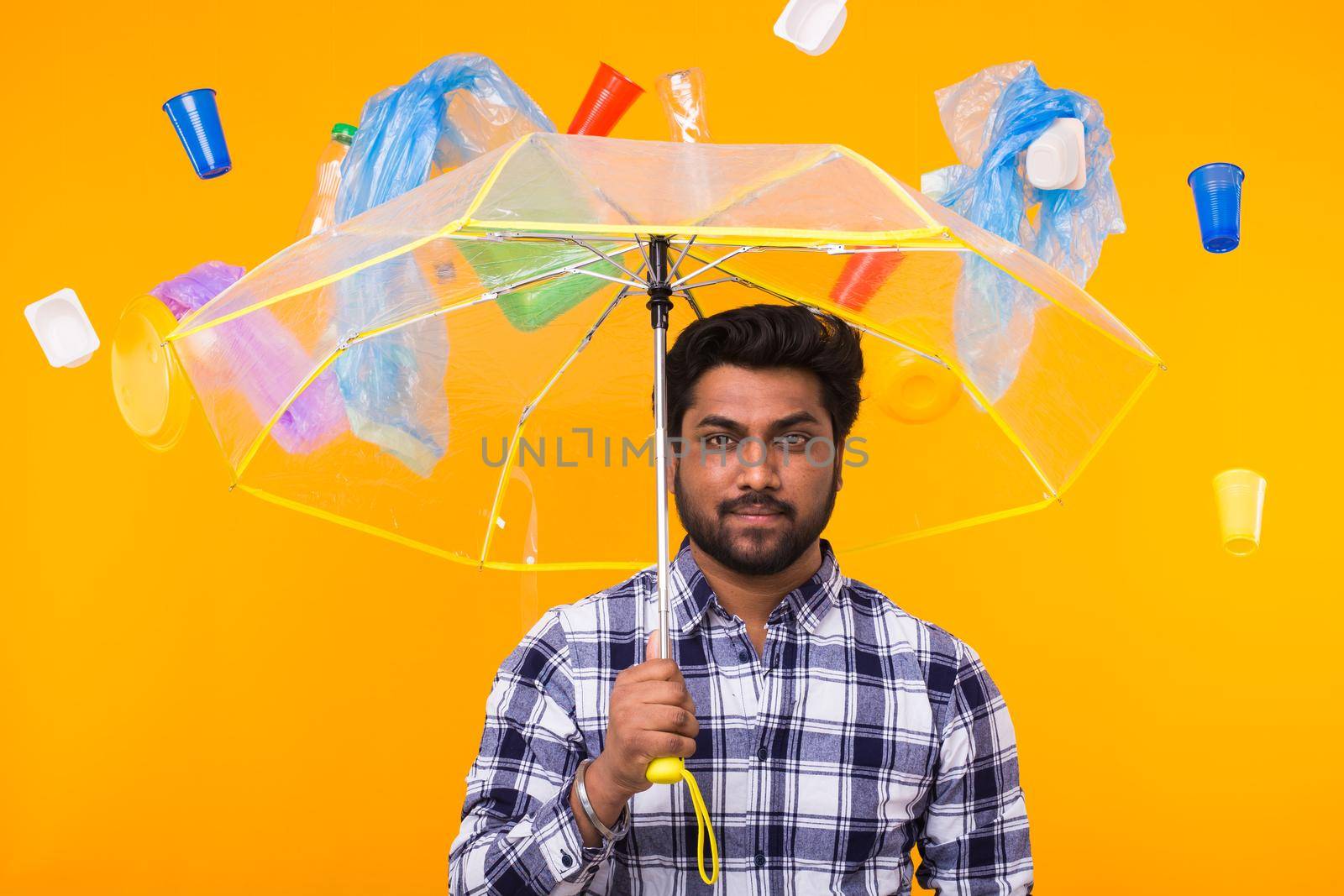 Plastic recycling problem, pollution and environmental disaster concept - Serious Indian man thinking about ecology under an umbrella on yellow background.