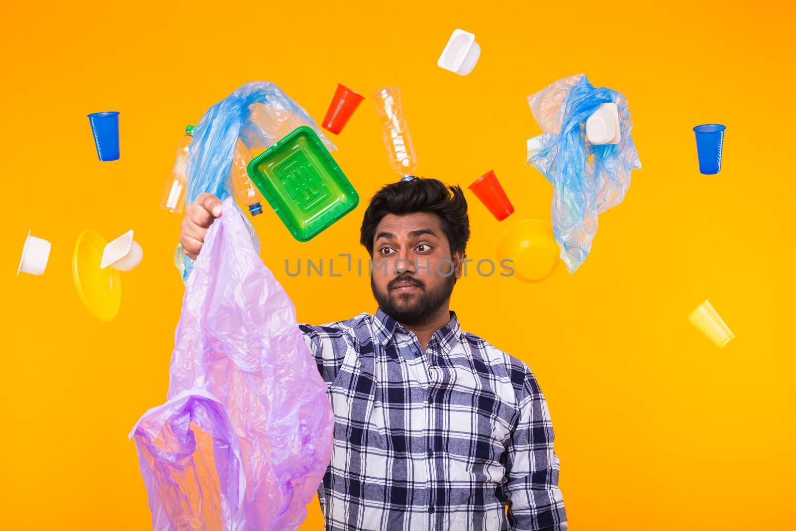 Plastic recycling problem, ecology and environmental disaster concept - Confused Indian man holding garbage bag on yellow background.