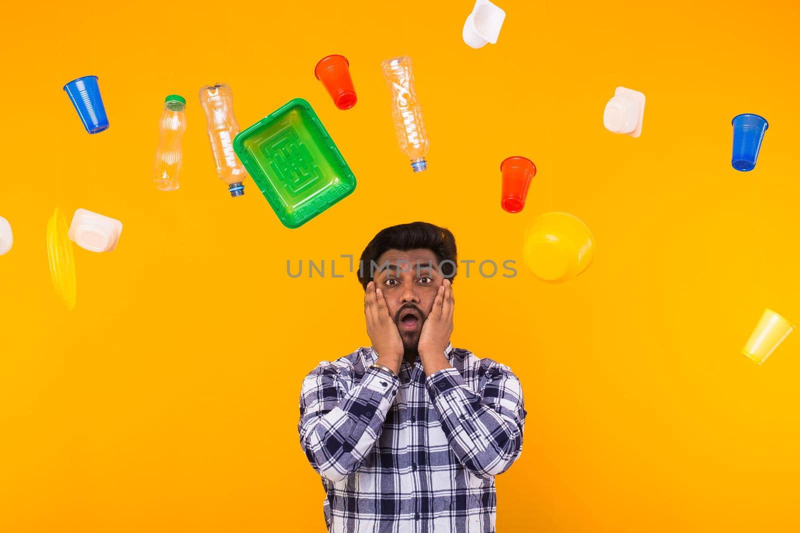 World Environment Day, plastic recycling problem and environmental disaster concept - Terrified Indian man on yellow background with trash.