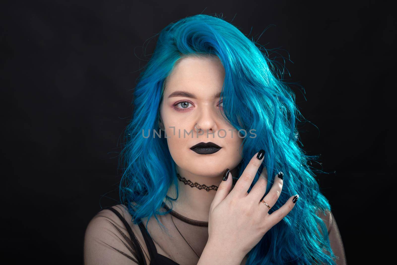 People and fashion concept - Young and attractive woman with black lipstick and blue hair posing over black background.