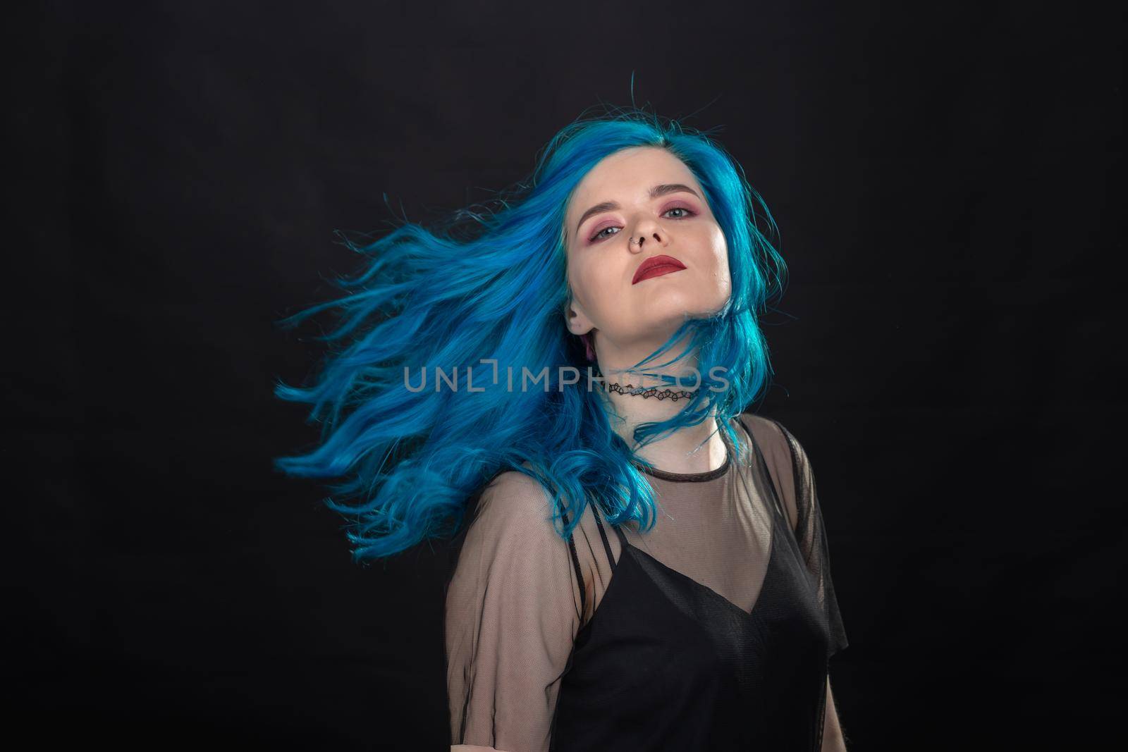 People and fashion concept - Young and attractive woman with black lipstick and blue hair posing over black background.