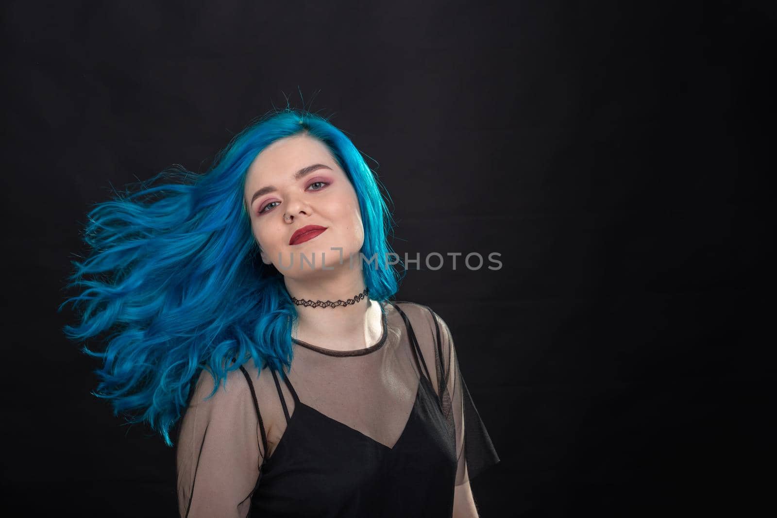 people, fashion and hair concept - close-up portrait of young woman in black dress with blue hair on black .