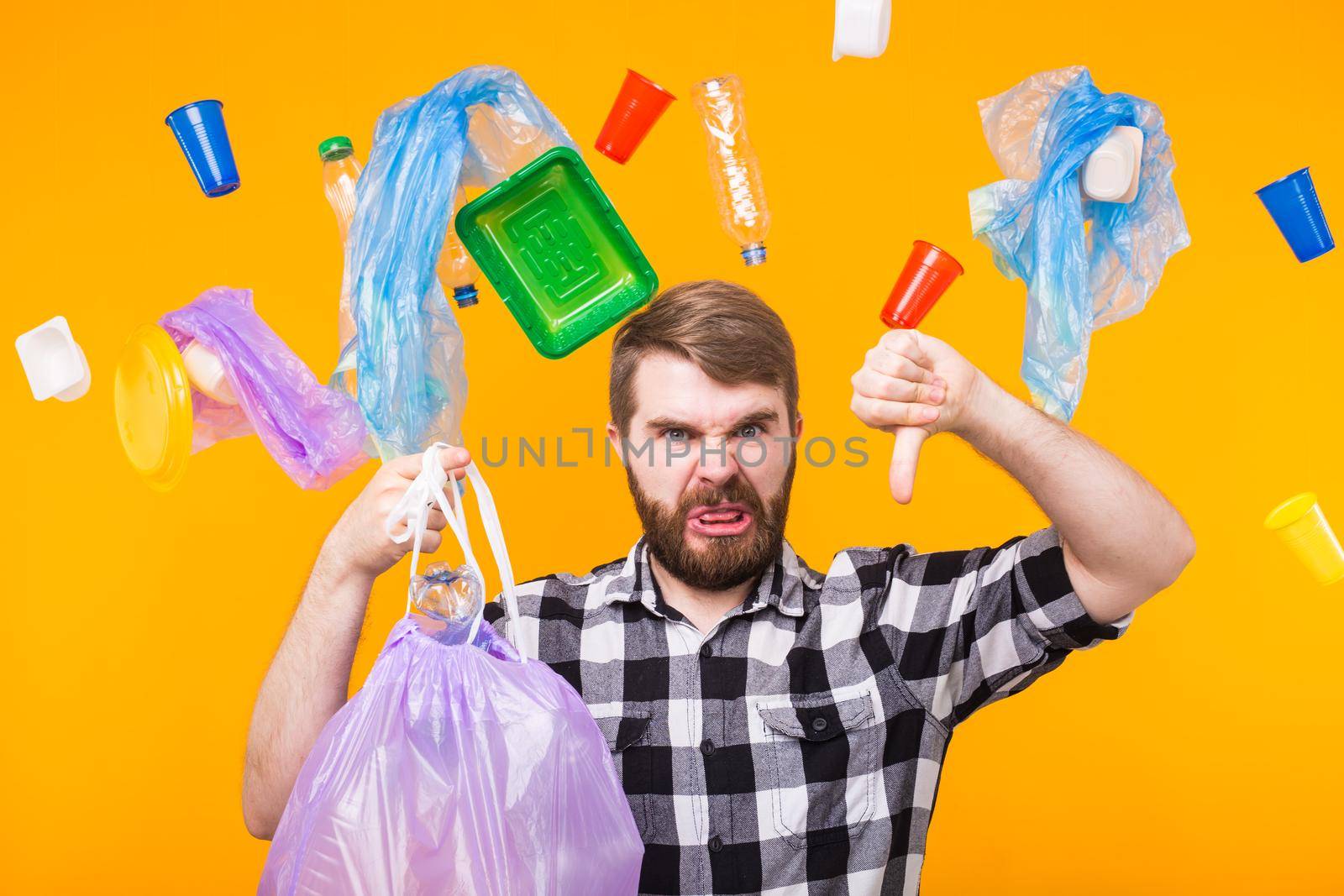 World Environment Day, plastic recycling problem and environmental disaster concept - Angry man holding garbage bag for recycling and showing thumb down on yellow background.
