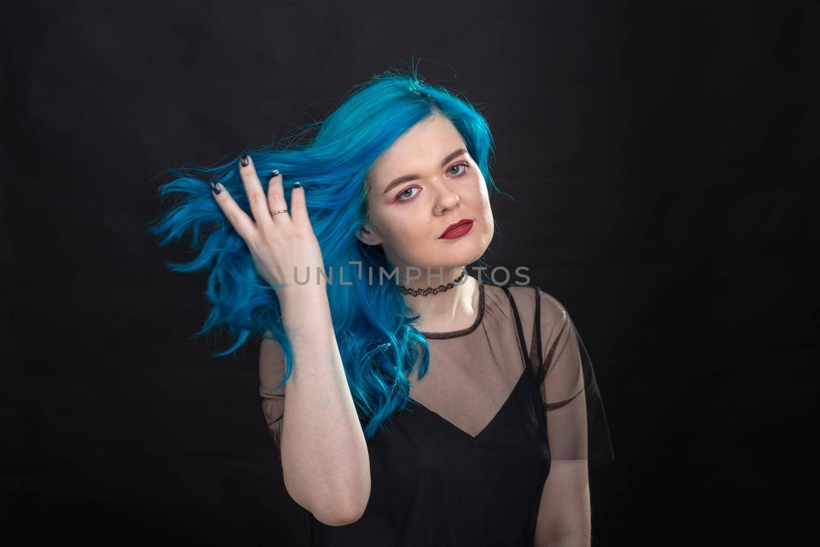 Style, fashion and hair concept - close-up portrait of young woman in black dress with blue hair on black background.