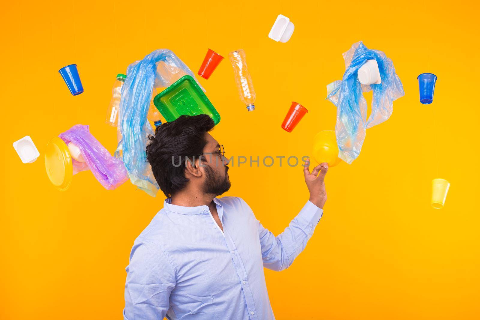 Environmental pollution, plastic recycling problem and waste disposal concept - surprised indian man holding garbage bag on yellow background
