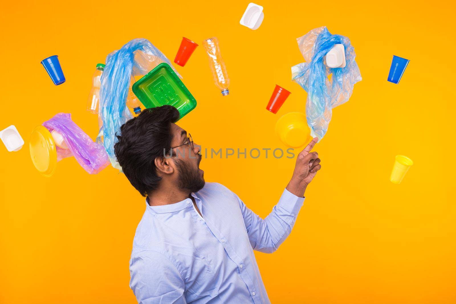 Environmental pollution, plastic recycling problem and waste disposal concept - Surprised Indian man point on trash on yellow background.