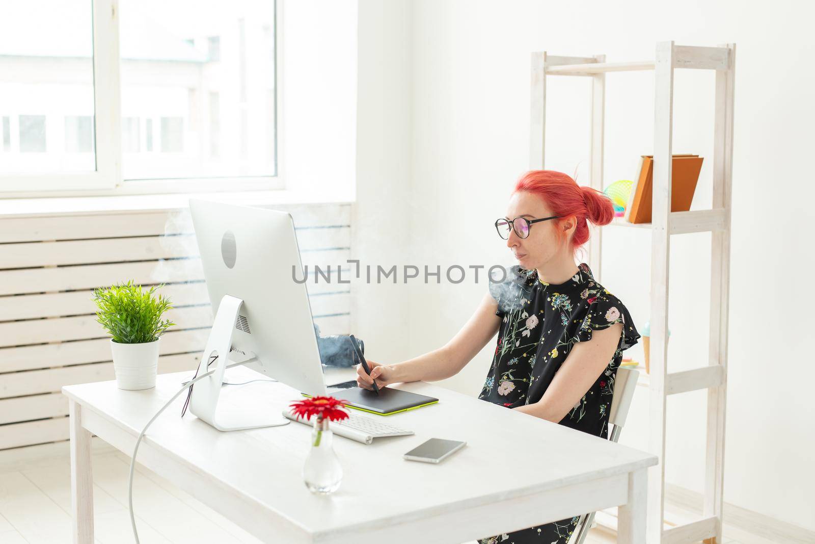 graphic designer concept - Female graphic designer working on computer while using graphic tablet at desk in the office and smoking a vape.