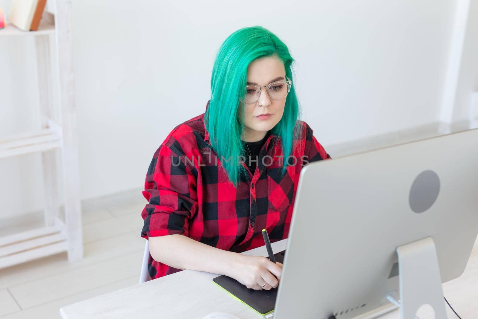 Designer, illustrator, artist and people concept - portrait of contemporary young woman with green hair using laptop and graphic tablet while working.