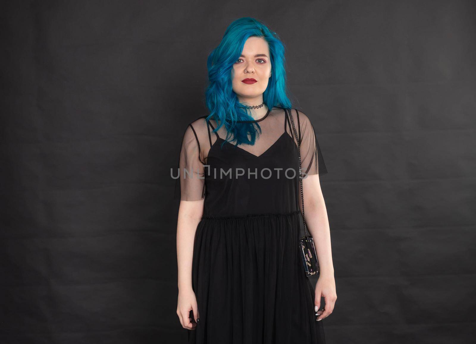 people, fashion and hair concept - full length portrait of young woman in black dress with blue hair on black background.