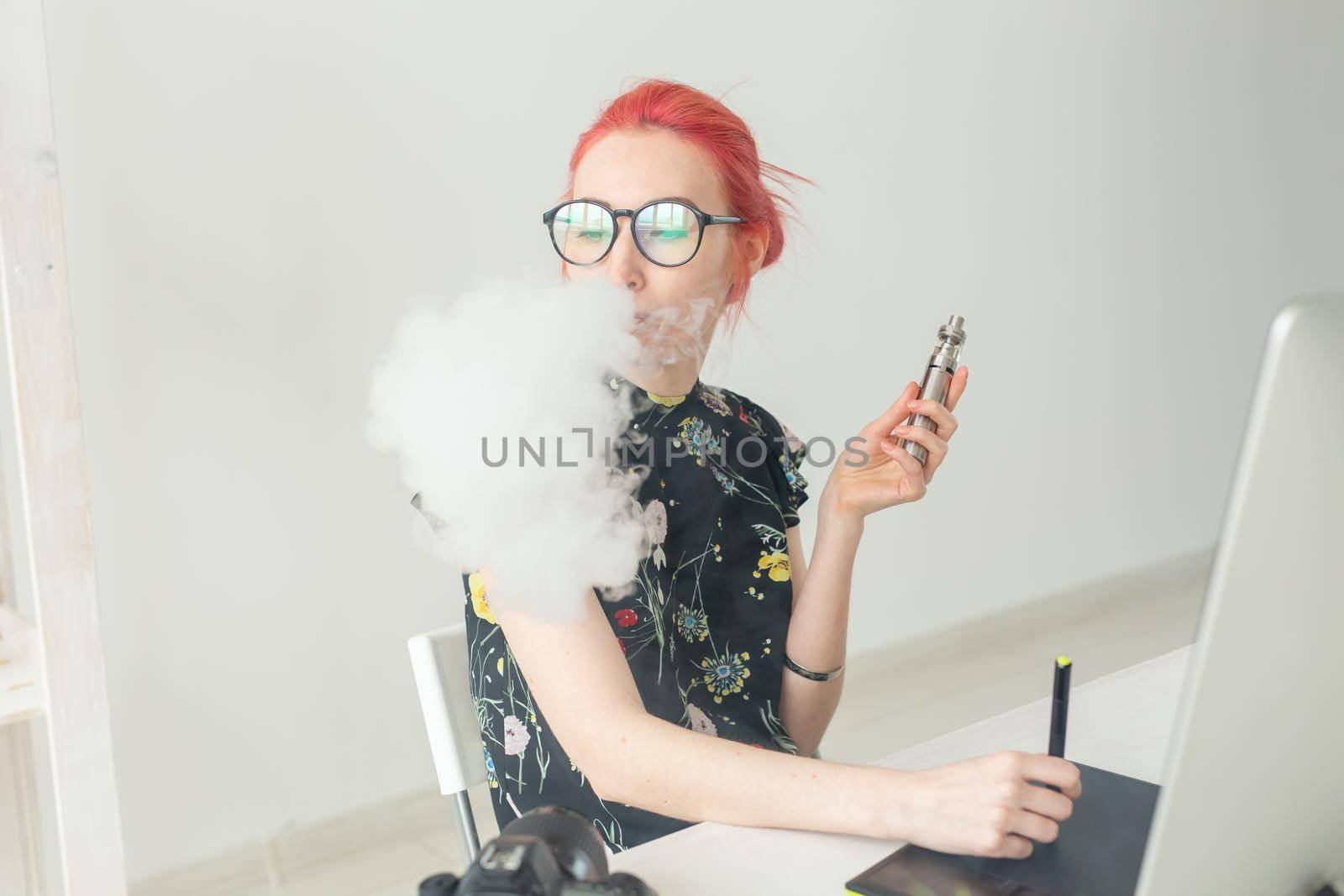 graphic designer concept - Female graphic designer working on computer while using graphic tablet at desk in the office and smoking a vape.