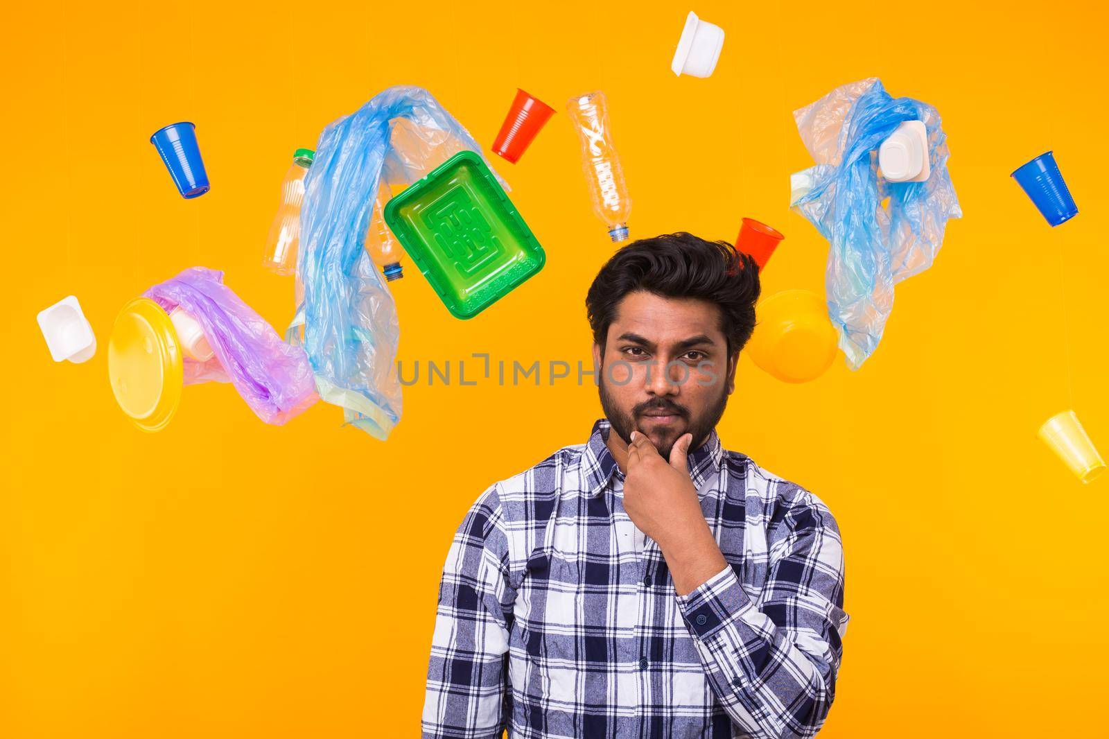 Problem of trash, plastic recycling, pollution and environmental concept - Serious Indian man looking forward on yellow background. He is thinking about ecology.