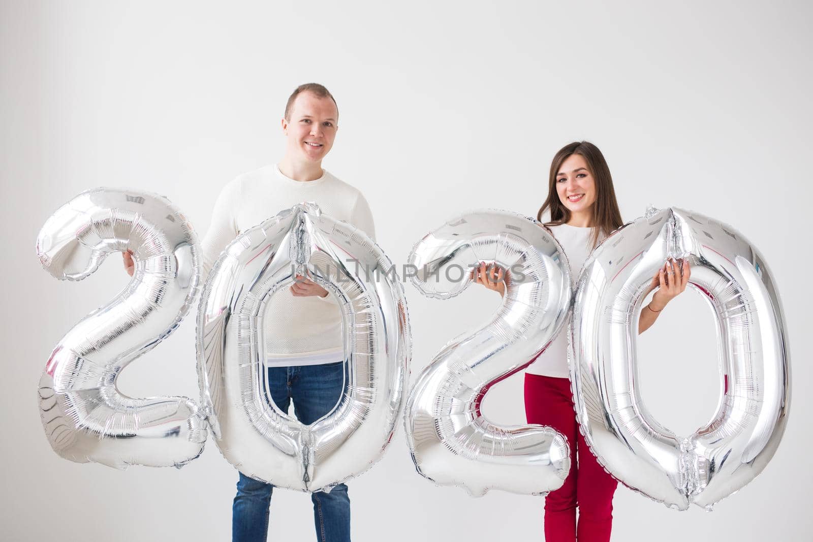 New year, celebration and holidays concept - love couple having fun with sign 2020 made of silver balloons for new year on white background by Satura86