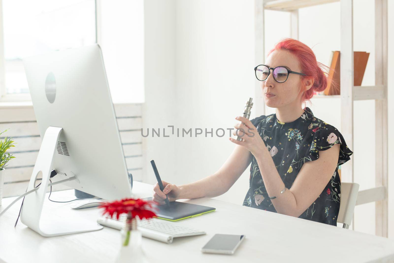 Creative, graphic designer, people concept - young creative woman smoking a vape while working in a graphic tablet.