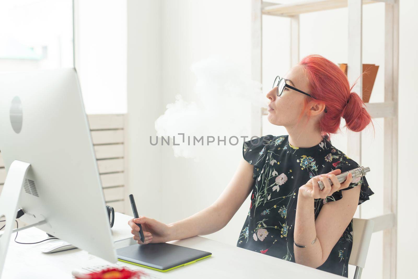 graphic designer concept - Female graphic designer working on computer while using graphic tablet at desk in the office and smoking a vape.