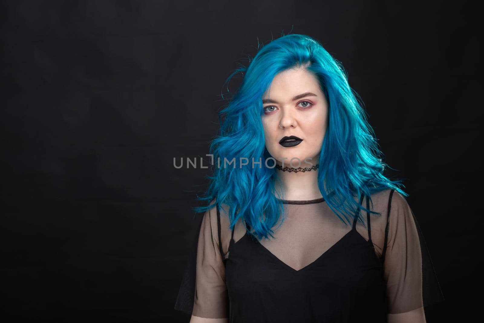 people, fashion and hair concept - close-up portrait of young woman in black dress with blue hair on black .