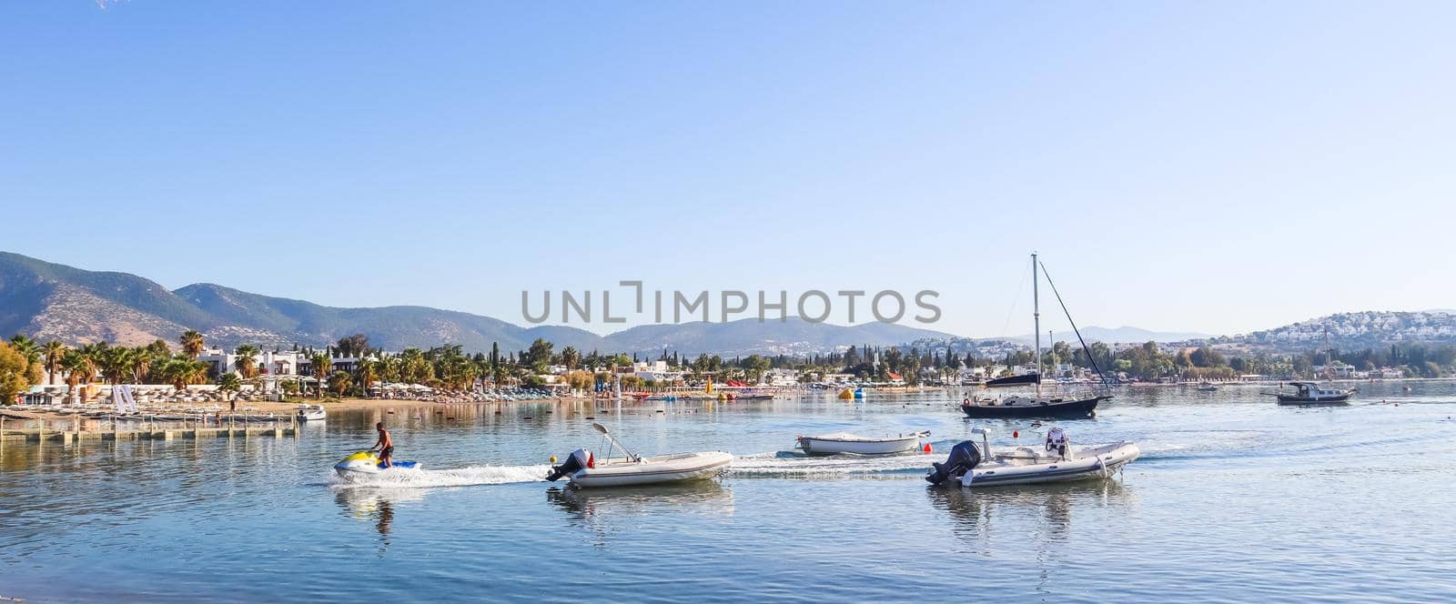 Beautiful bay with calm water, sandy beach, boats and yachts. Small town and green mountains on the coast of the Aegean sea