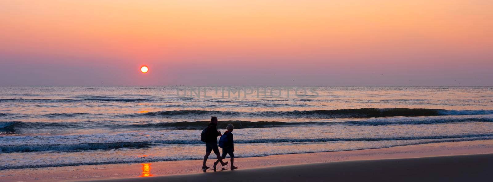 mother and child walk on beach during colorful sunset over north sea by ahavelaar