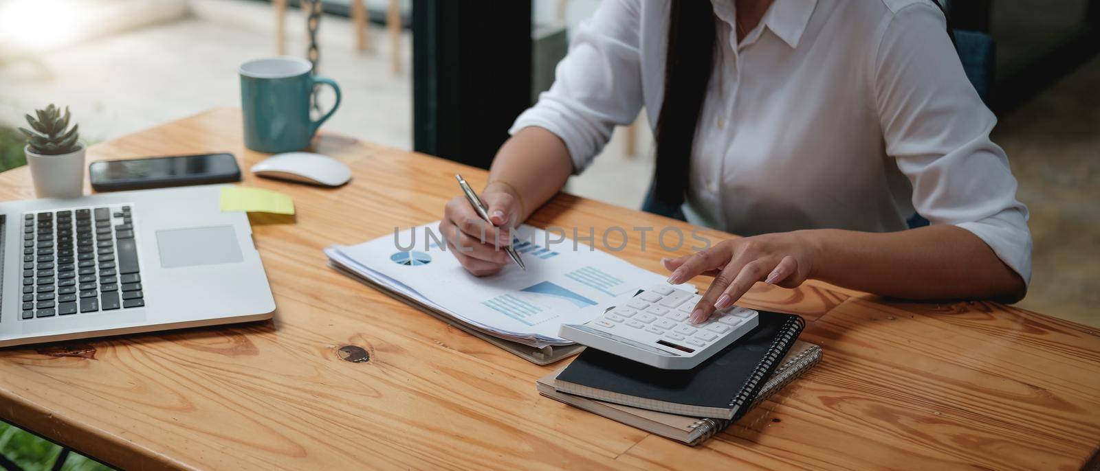 Close up asian female accountant or banker making calculations with calculator. Savings, finances and economy concept through a laptop by nateemee