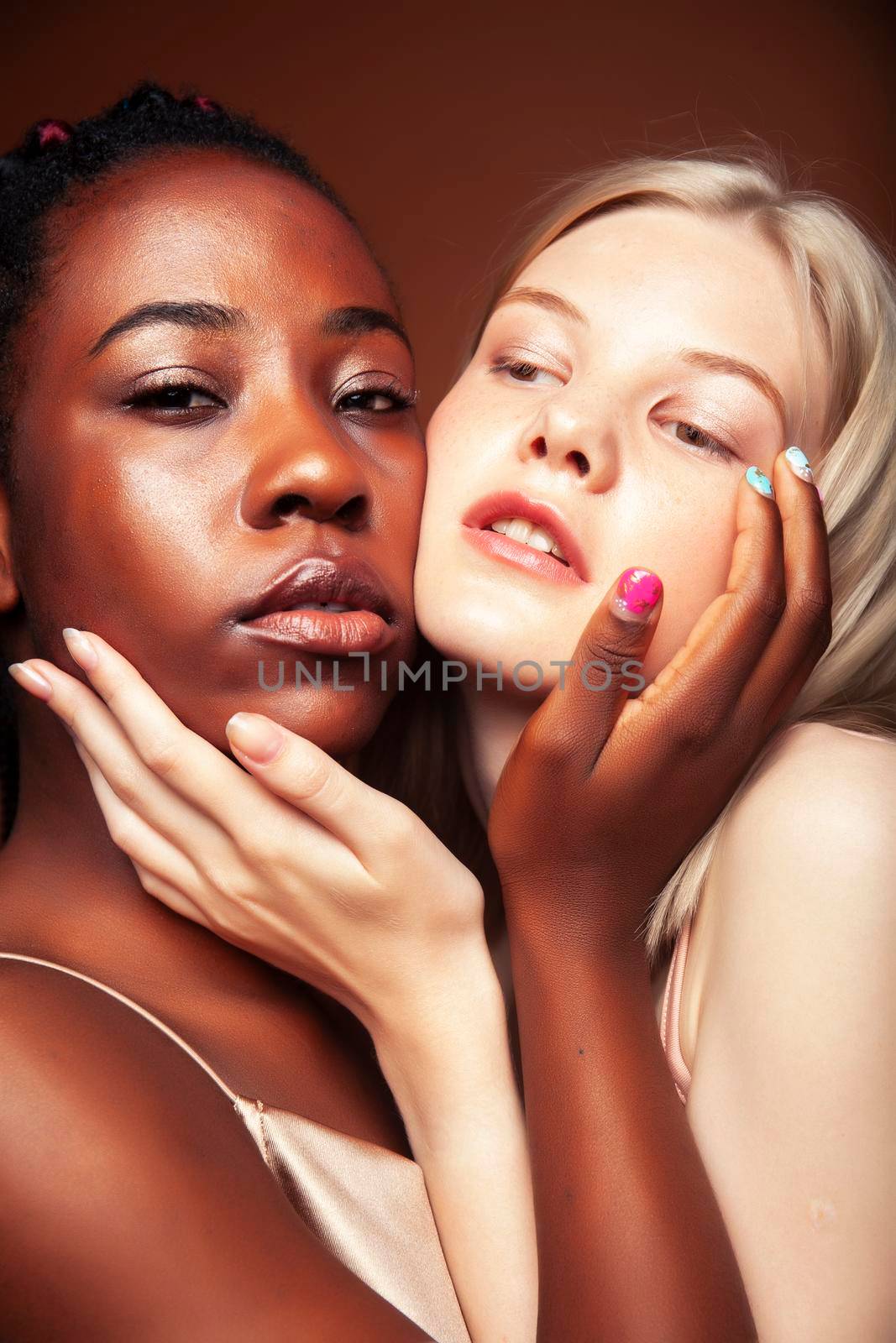 two pretty girls african and caucasian blond posing cheerful together on brown background, ethnicity diverse lifestyle people concept by JordanJ