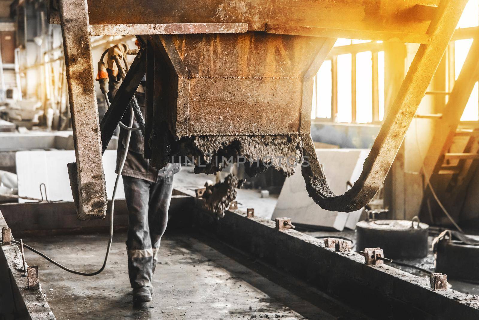 A construction worker controls the flow of concrete and gravel mix from a mixer in a rebar shop of an industrial plant, selective focus by AYDO8