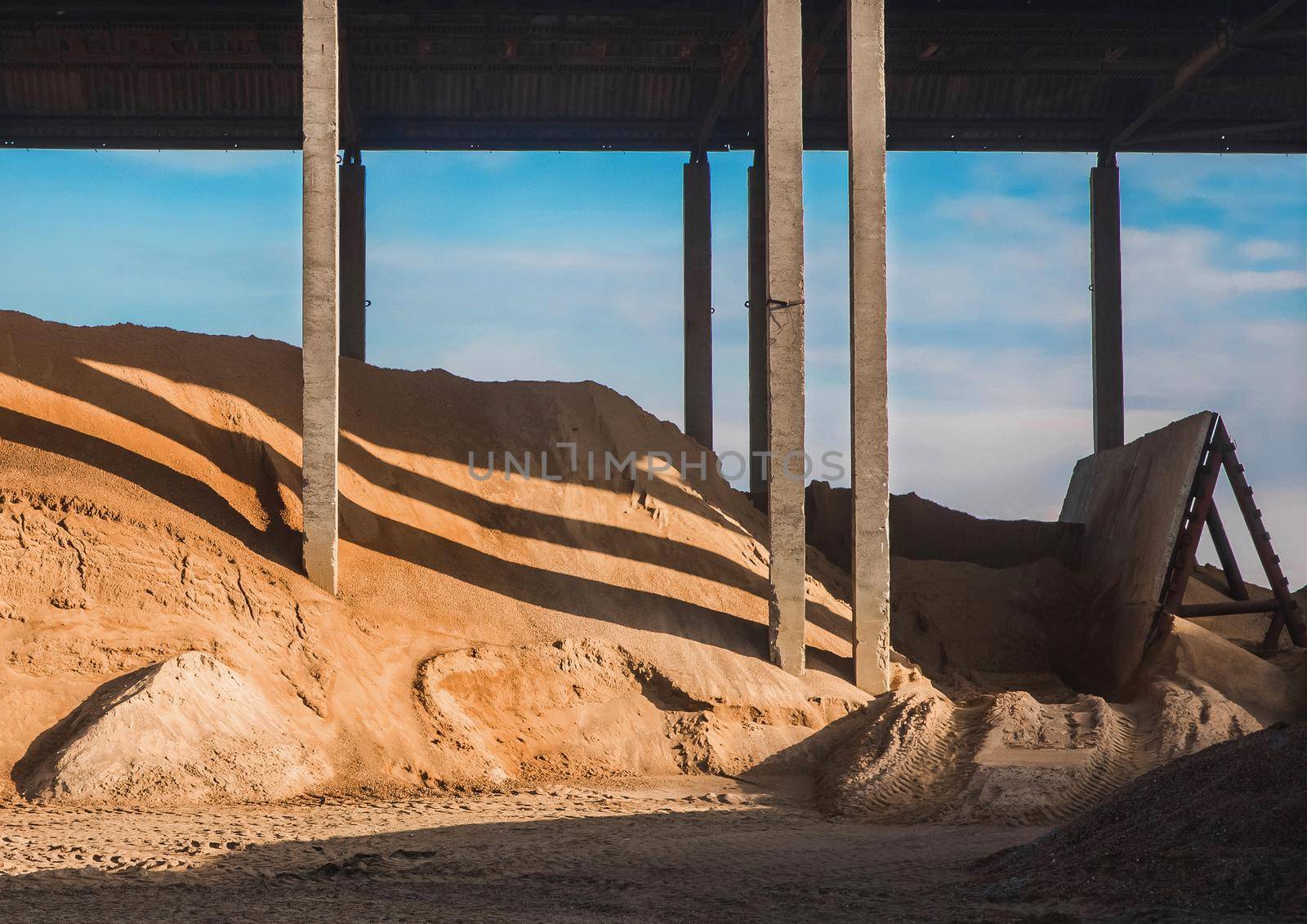 A large pile of sand under a canopy of slate storage on industrial warehouse at a construction site.