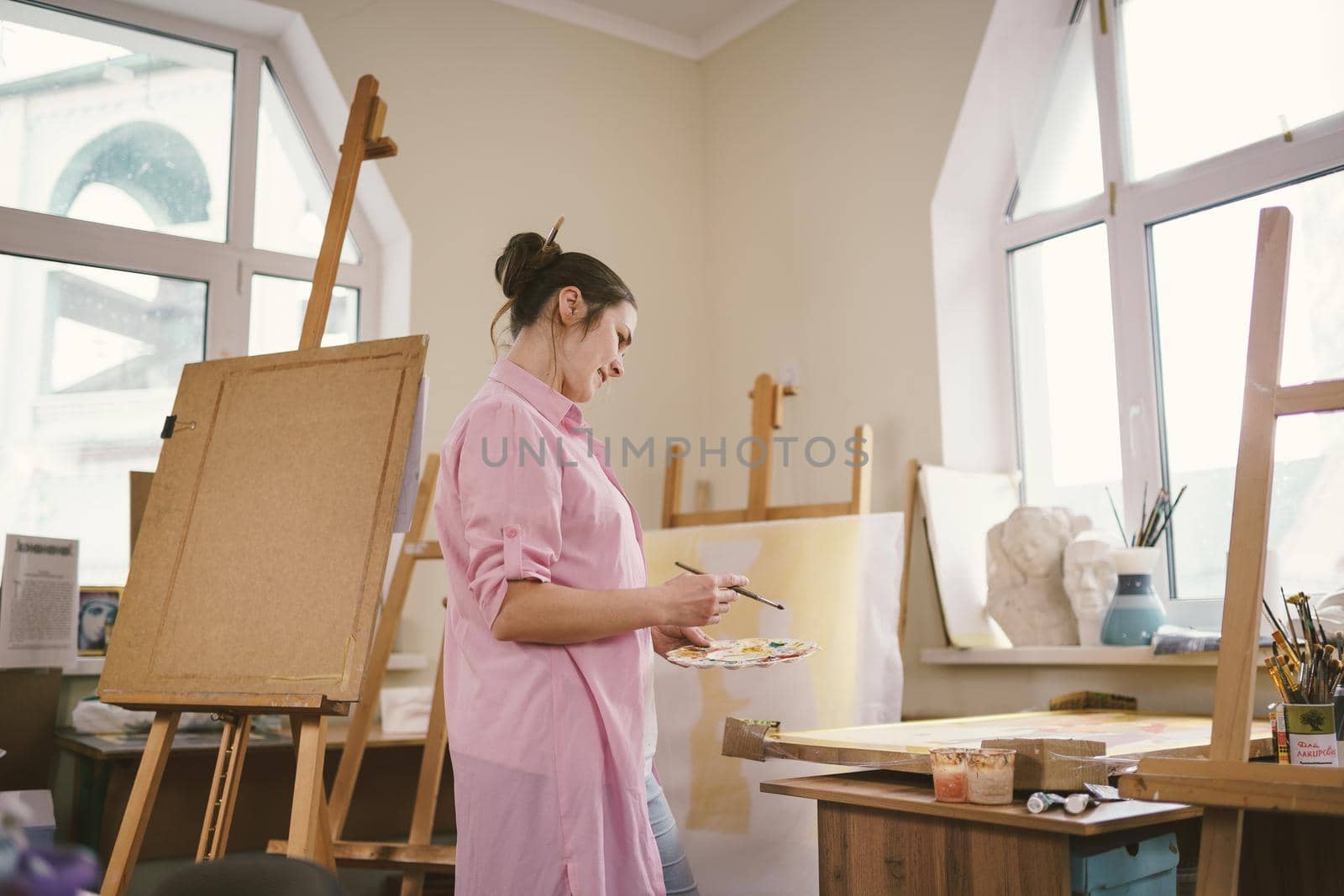 Female artist working in studio. Creative workspace, painting class, easel with canvas, art therapy. Inspiration, creativity, talent, craft concept. Artist studio interior. People, leisure and hobby by Tomashevska