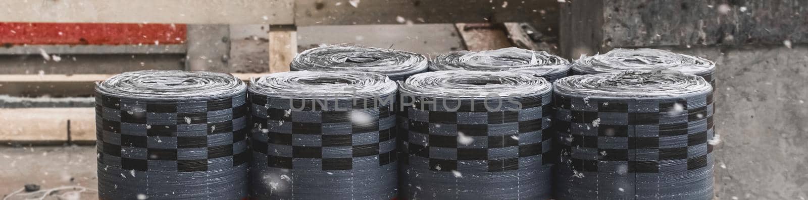 Pile of rolls of dark thermal insulation industrial materials storage outdoor on a construction site during a snowfall.