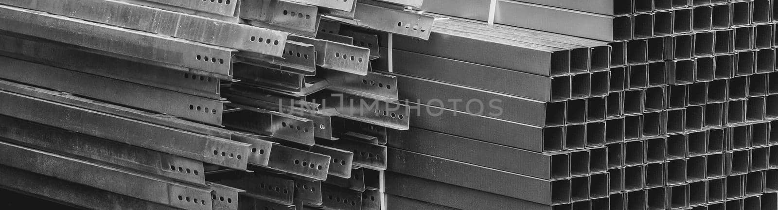 A pile of metal plates and square industrial pipes. Building materials at the construction site.