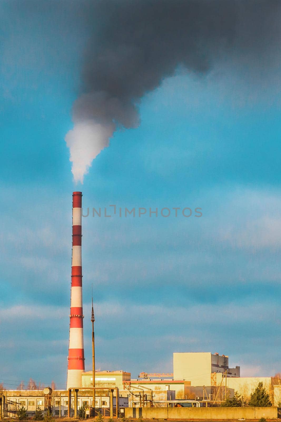 Environmental pollution, environmental problem, smoke from the pipe of an industrial plant or thermal power plant against a blue sky and sunset.