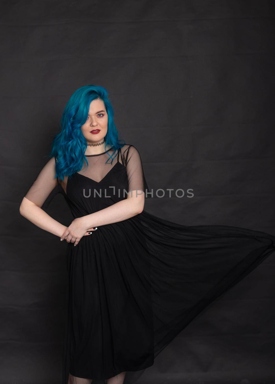 People and fashion concept - Woman dressed in black dress and blue hair posing over black background.