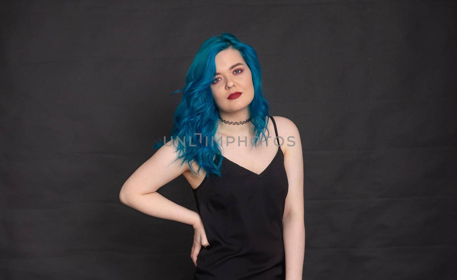 People and fashion concept - Woman dressed in black dress and blue hair posing over black background.
