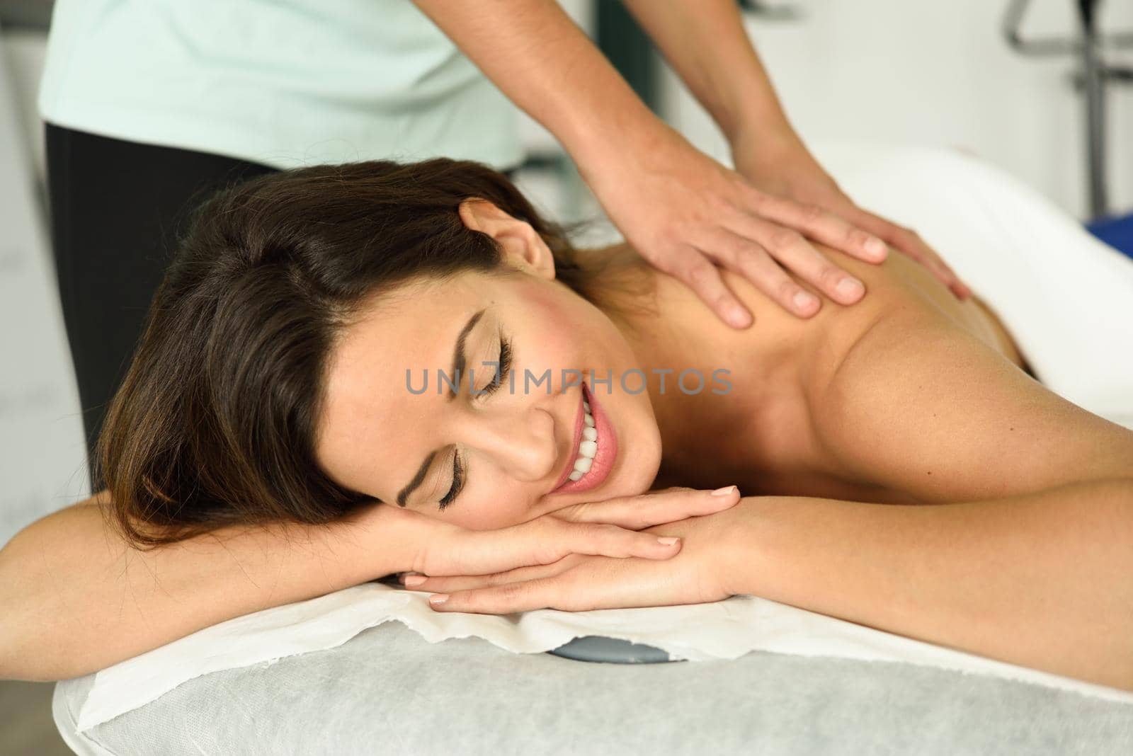 Young female receiving a relaxing back massage in a spa center. Brunette woman patient is receiving treatment by professional therapist.
