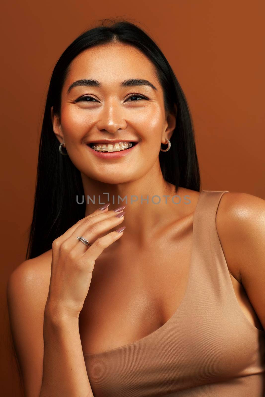 young pretty asian woman cheerful smiling posing on warm brown background, lifestyle people concept close up