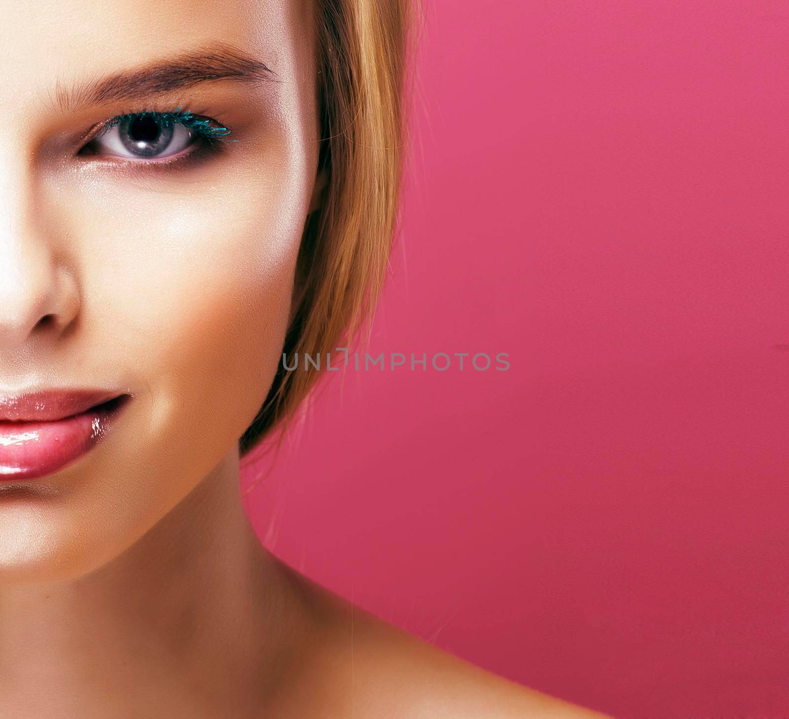 young pretty blonde real woman with hairstyle close up and makeup on pink background smiling close up