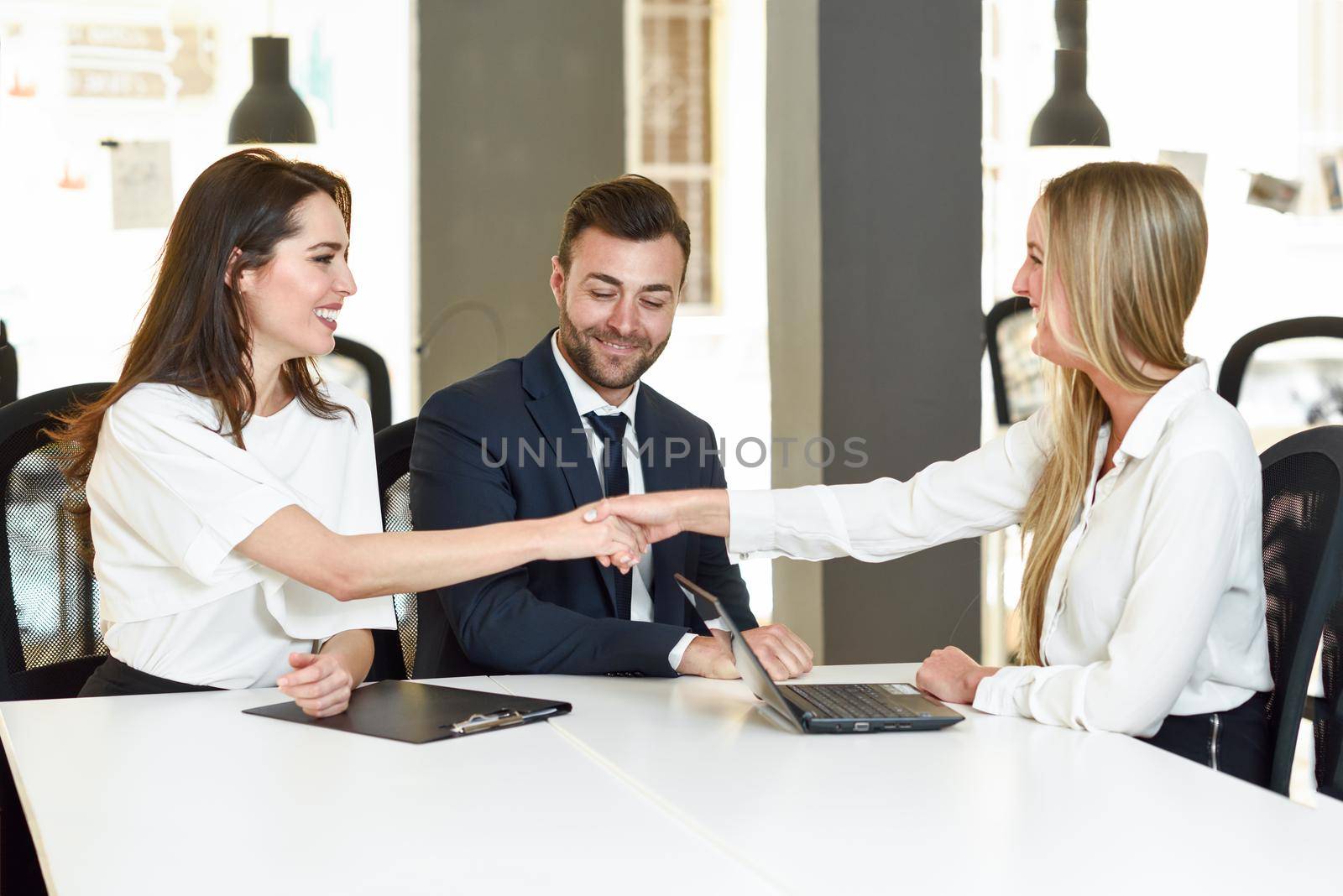 Smiling young couple shaking hands with an insurance agent or investment adviser. Three people meeting in an office reaching an agreement