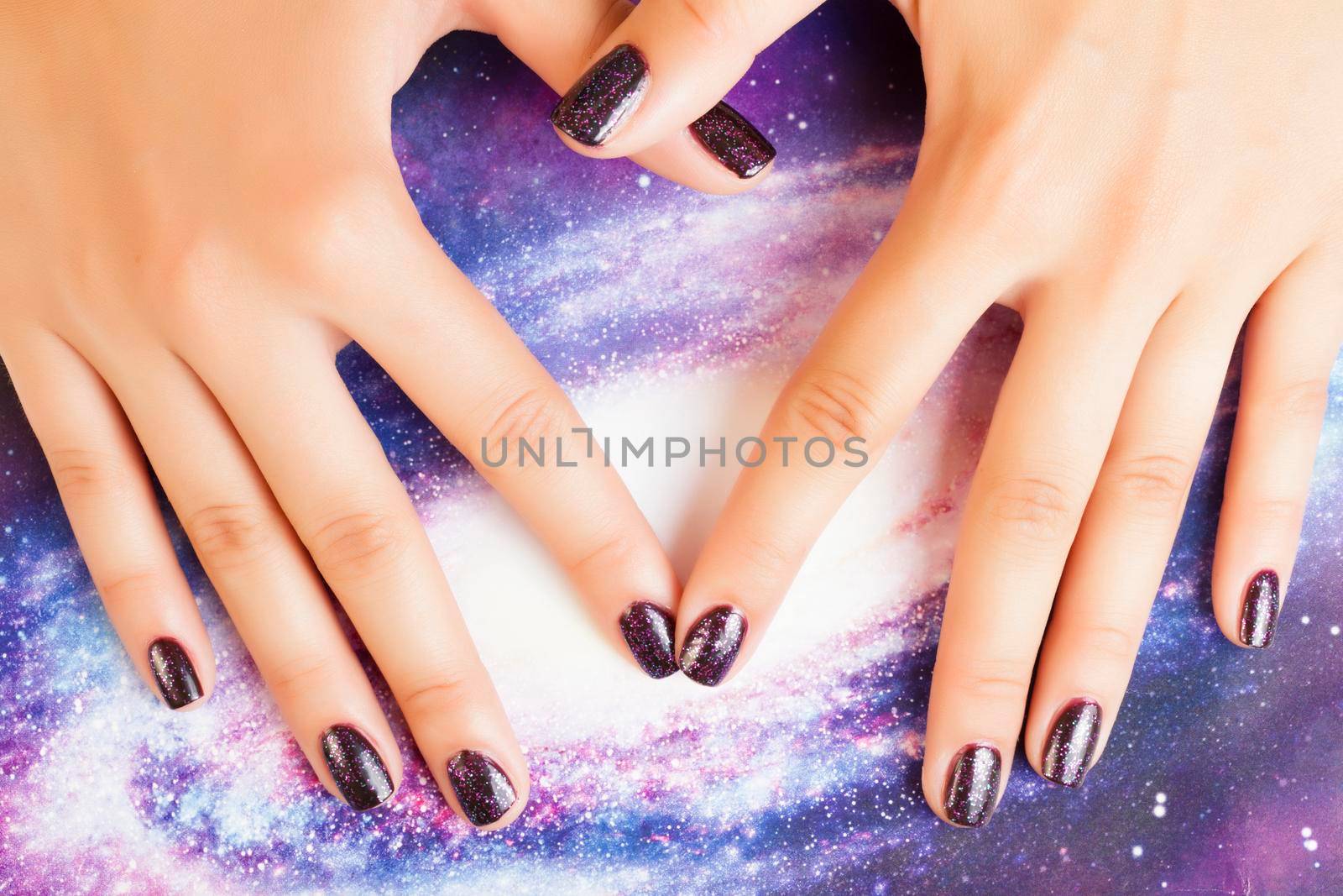 manicure stylish concept: woman fingers with nails purple glitter on nails like cosmos, universe background close up