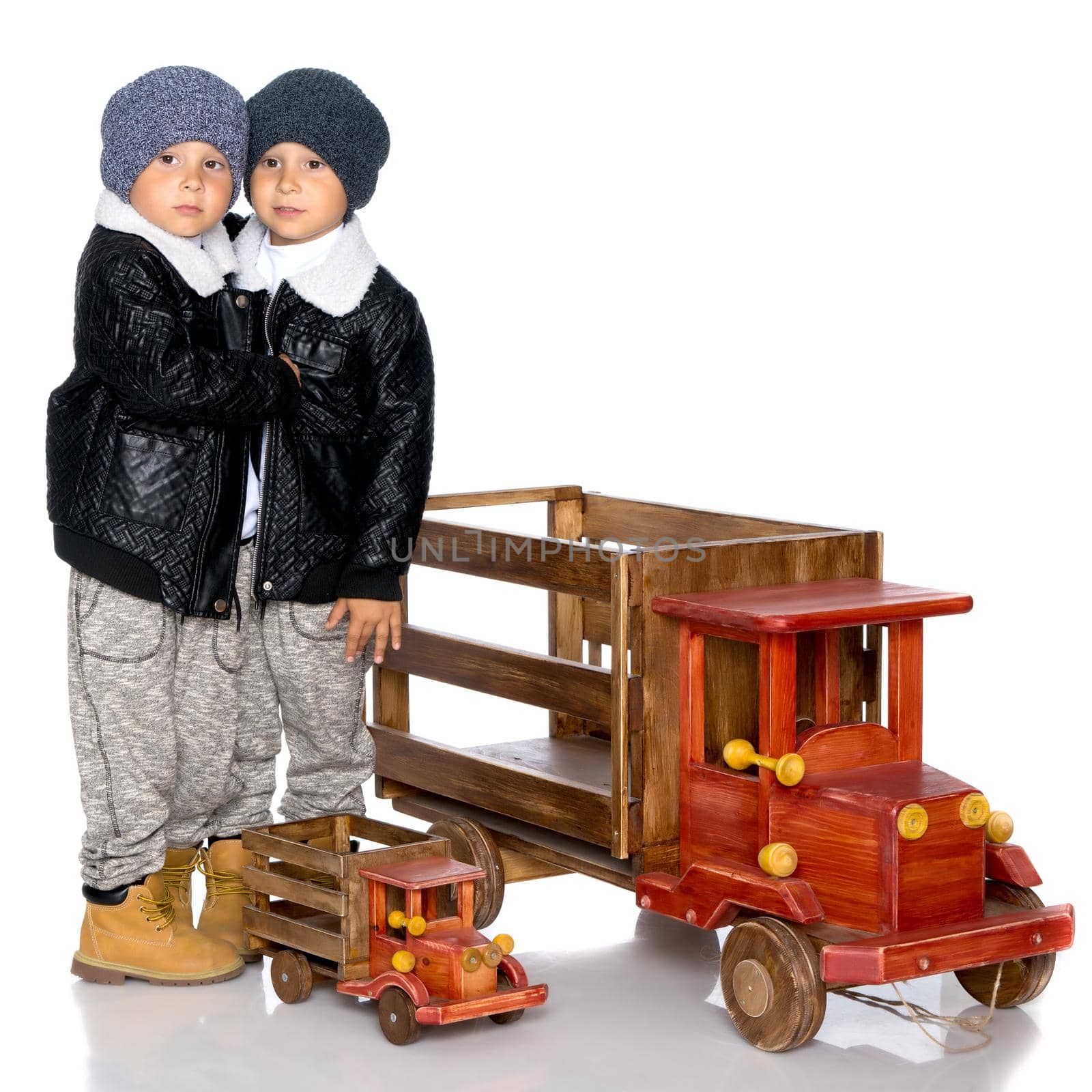 Two little boys play with wooden cars. In autumn jackets and hats. Isolated on white background.