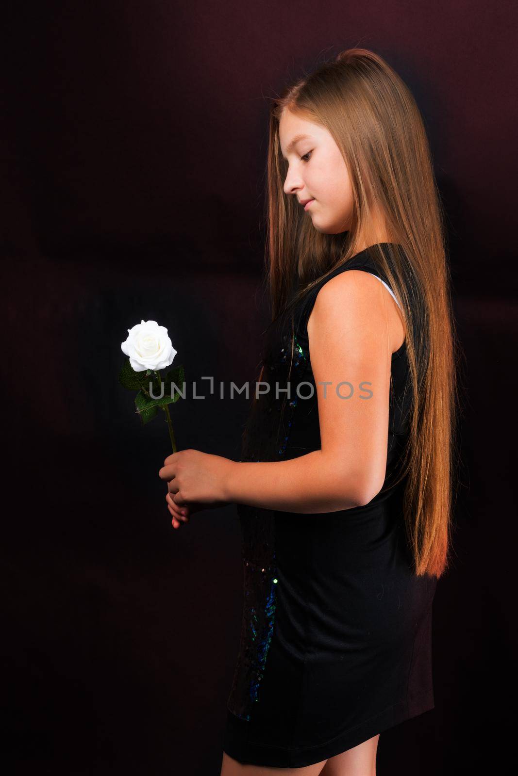 A teenage girl with a flower in her hand. Shooting in the studio on a black background.