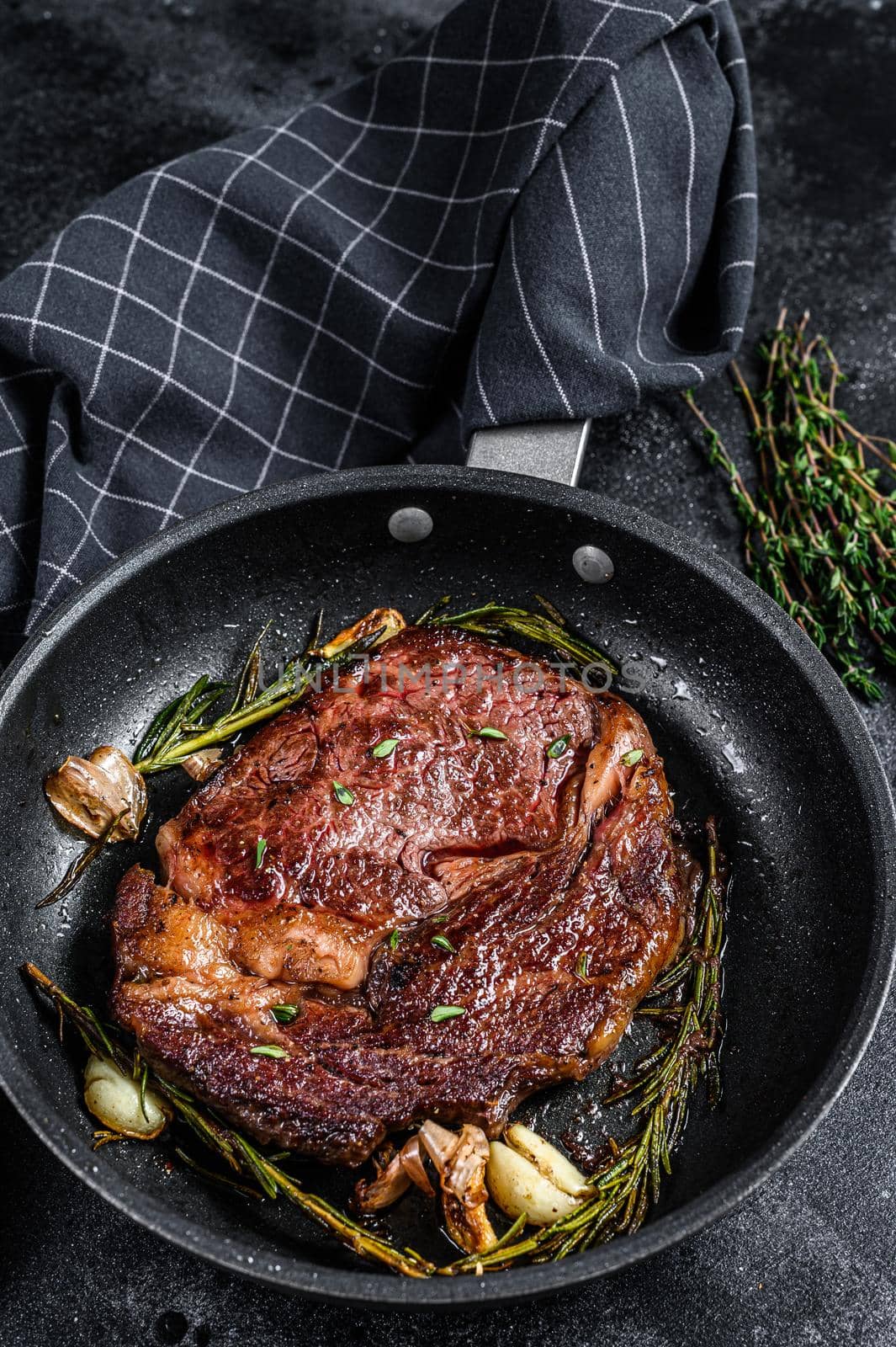 Roasted rib eye steak, ribeye beef meat in a pan. Black background. Top view.