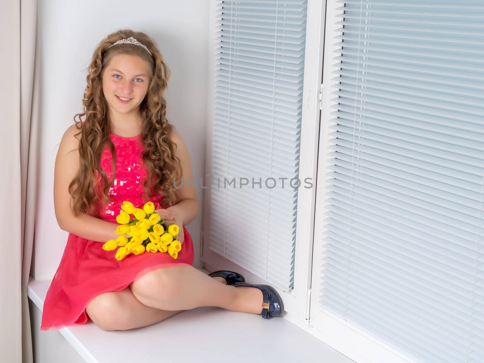 A nice little girl sits on a window sill with a bouquet of tulips. The concept of happy people, spring vacation.