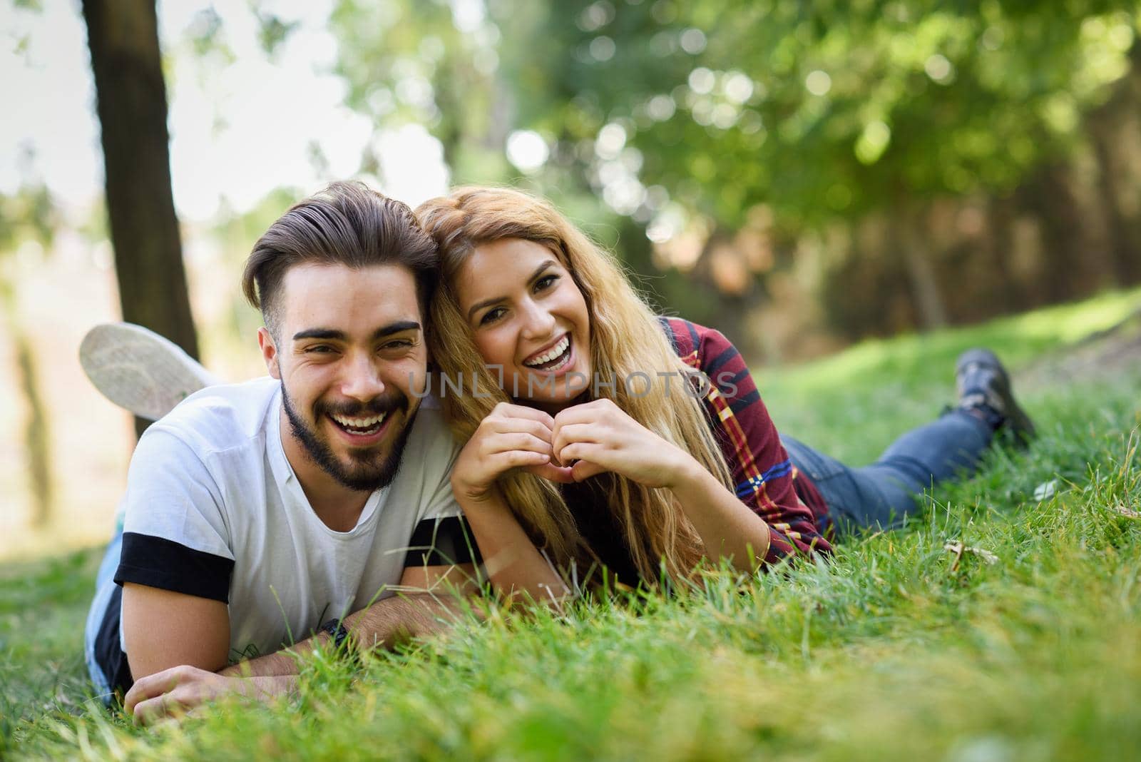 Beautiful young couple laying on grass in an urban park. Caucasian man and woman wearing casual clothes. Blonde female.