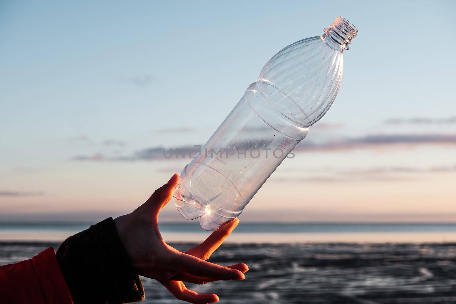 A human hand holds a plastic bottle thrown on the shore by vollirikan