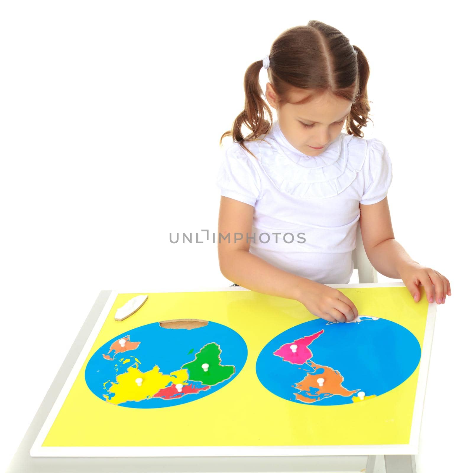 A little girl in Montessori kindergarten sits at a table and studies Montessori stuff. The concept of school and preschool education, harmonious development of the child. Isolated on white background.