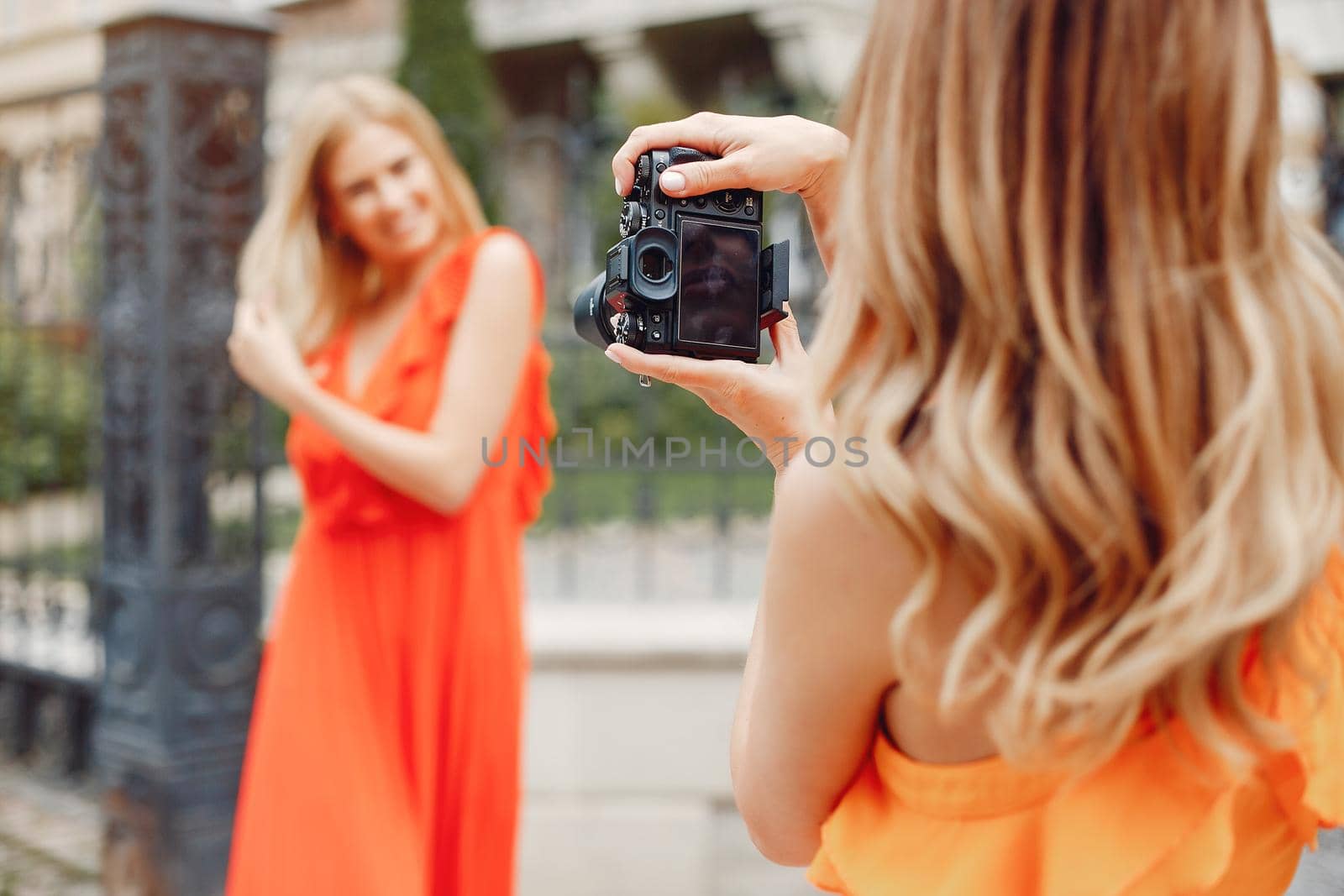 Beautiful girl in a red dress. Women in a summer city. Lady make a photo for her girlfriend