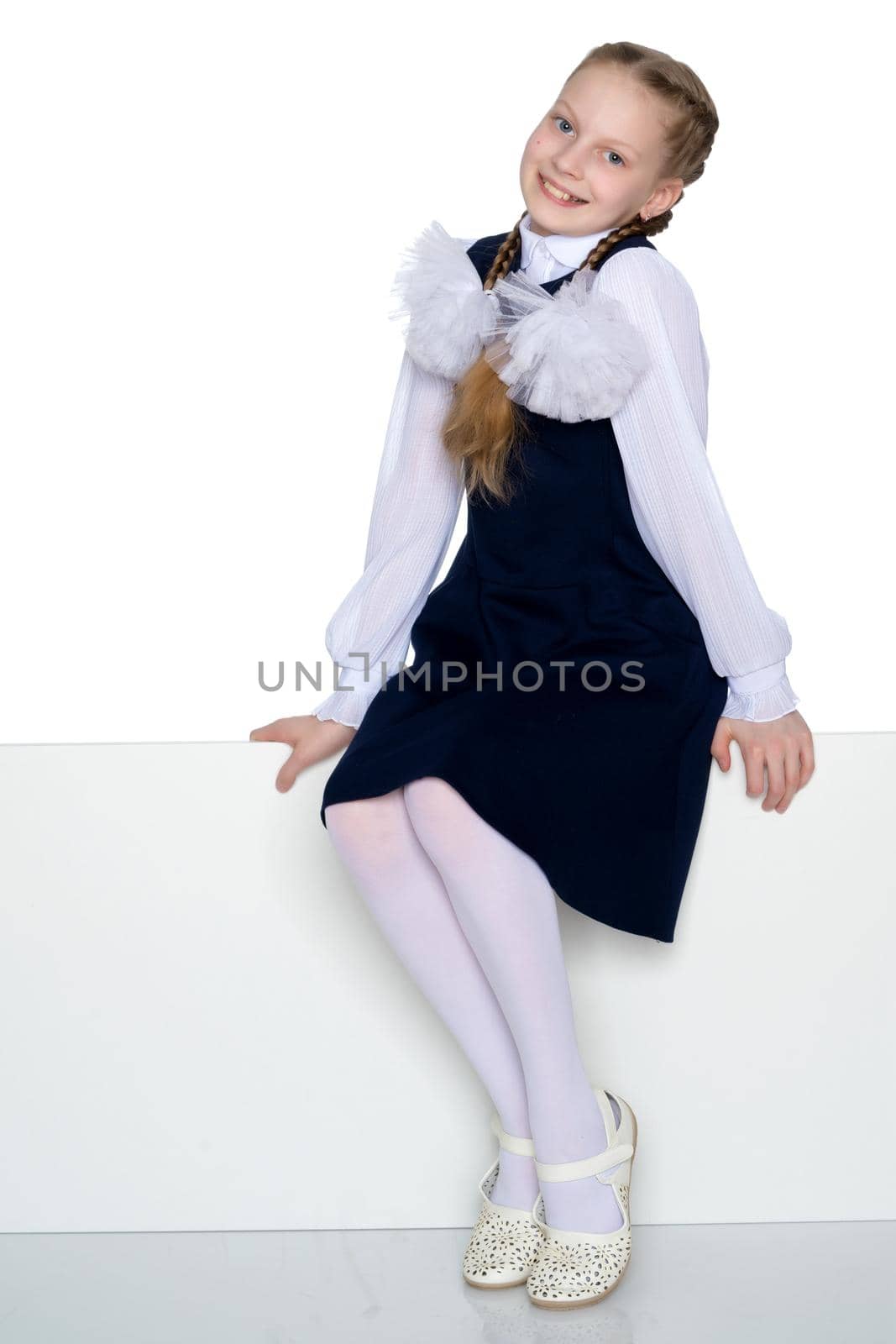 Beautiful schoolgirl girl with long pigtails sitting on the couch. The concept of school fashion, children's emotions. Isolated on white background.