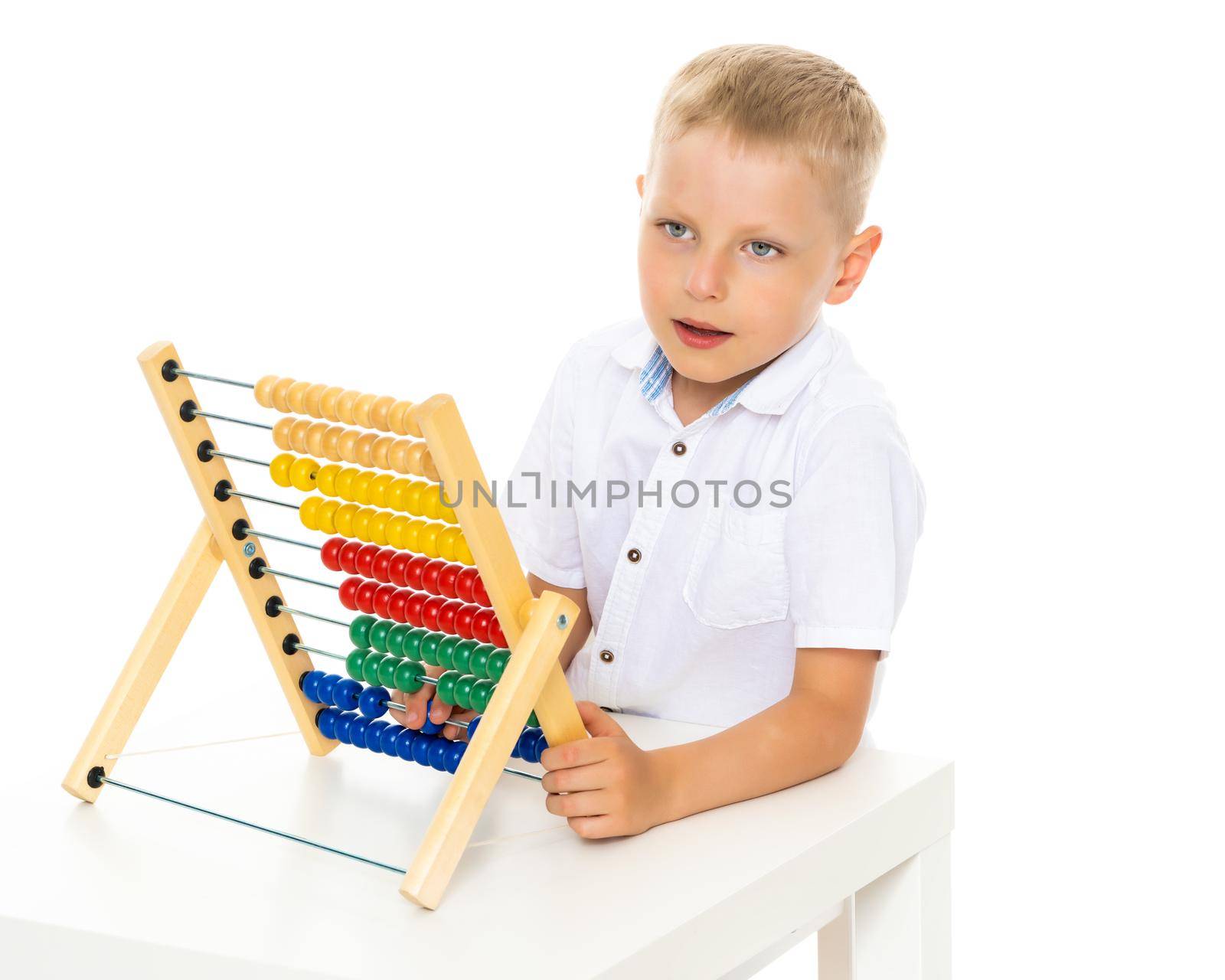 A cute little boy at school at a table studying mathematics. He uses abacus to solve mathematical problems. The concept of teaching a child in the family or at school.Isolated on white background.